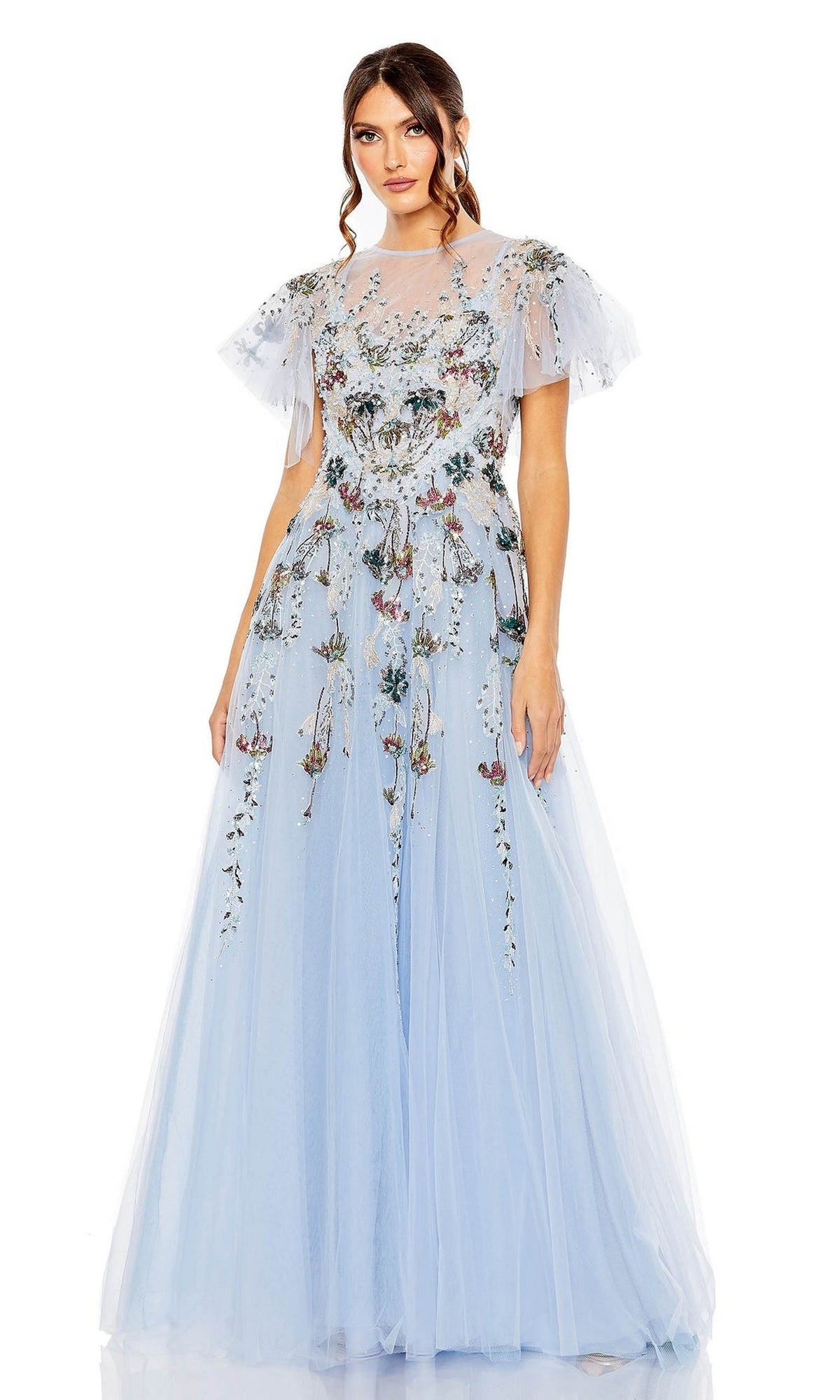 A woman models the Long Formal Dress 20436 by Mac Duggal—an embroidered, light blue tulle A-line gown with floral accents, short flutter sleeves, and a sheer neckline—standing against a white background.